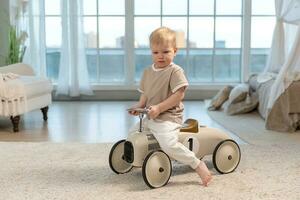 contento niño a hogar. pequeño niñito chico conducción grande Clásico juguete coche y teniendo divertida. sonriente niño jugando a hogar. bebé chico jugando con juguete en vivo habitación adentro. foto