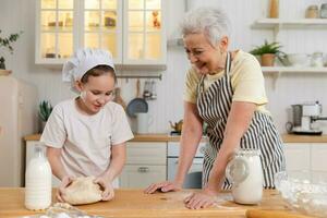 Happy family in kitchen. Grandmother and granddaughter child cook in kitchen together. Grandma teaching kid girl knead dough bake cookies. Household teamwork helping family generations concept. photo