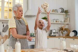 Happy family in kitchen. Grandmother and granddaughter child cook in kitchen together. Grandma teaching kid girl knead dough bake cookies. Household teamwork helping family generations concept. photo