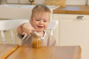 Happy family at home. Baby boy feeding himself in kitchen. Little boy with messy funny face eats healthy food. Child learns eat by himself holding spoon. Self feeding. photo