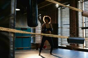 mujer yo defensa niña fuerza. africano americano mujer combatiente formación puñetazos en boxeo anillo. sano fuerte niña puñetazos boxeo bolsa. formación día en boxeo gimnasia. fuerza ajuste cuerpo rutina de ejercicio capacitación. foto