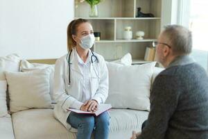 Female doctor examining older senior man in doctor office or at home. Old man patient and doctor have consultation in hospital room. Medicine healthcare medical checkup. Visit to doctor. photo