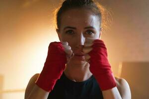 Women self defense girl power. Strong woman fighter punching with red boxing wraps sports protective bandages. Girl punching training punches looking concentrated straight. Fit body workout. photo