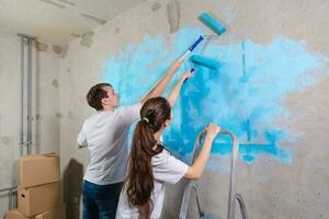 Pareja en nuevo hogar durante reparar trabajos pintura pared juntos. contento familia participación pintar rodillo pintura pared con azul color pintar en nuevo casa. hogar renovación bricolaje renovar hogar concepto. foto