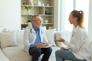 Senior man doctor examining yound woman in doctor office or at home. Girl patient and doctor have consultation in hospital room. Medicine healthcare medical checkup. Visit to doctor. photo