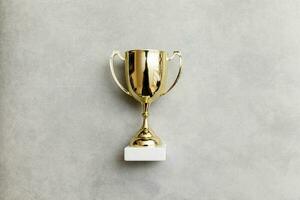 Simply flat lay design winner or champion gold trophy cup on concrete stone grey background. Victory first place of competition. Winning or success concept. Top view copy space. photo