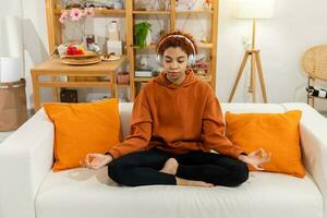 Yoga mindfulness meditation. Young healthy african girl practicing yoga at home. Woman sitting in lotus pose on yoga mat meditating smiling relaxing indoor. Girl doing breathing practice, yoga at home photo