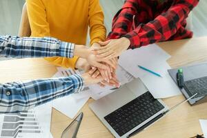 apilar de manos. negocio puesta en marcha trabajo en equipo unidad concepto. diverso equipo poniendo su manos juntos parte superior vista. joven personas grupo negocio colegas sentado en oficina, trabajo proceso éxito de compañía. foto