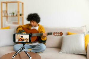 Blogger guitarist. Happy african american girl blogger playing guitar singing song recording vlog. Social media influencer woman streaming recording at home studio. Music content creator broadcast. photo