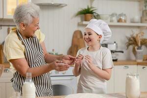 Happy family in kitchen. Grandmother and granddaughter child cook in kitchen together. Grandma teaching kid girl knead dough bake cookies. Household teamwork helping family generations concept. photo