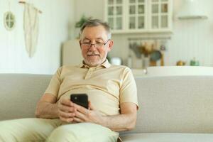 Happy middle aged senior man holding using smartphone touch screen typing scroll page. Stylish older mature beard grandfather with cell phone using internet social media apps at home. Shopping online. photo