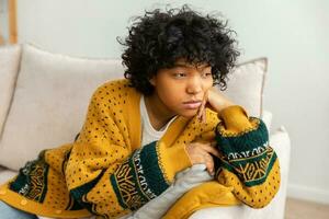 africano americano triste pensativo pensativo desmotivado niña sentado en sofá a hogar interior. joven africano mujer reflexionar Mira cansado después largo día. niña siente Deprimido ofendido solitario trastornado desamor foto