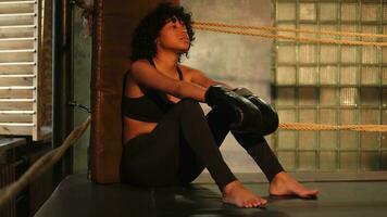 Woman fighter girl power. African american woman fighter with boxing gloves sitting on boxing ring waiting and resting after fight. Strong powerful girl in gym. Strength fit body workout training. photo