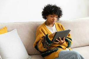 African american girl holding digital tablet touch screen typing scroll page at home. Woman with mobile tech device surfing internet using social media apps playing game. Study work shopping online. photo