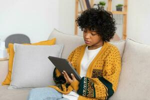 niña afroamericana sosteniendo la pantalla táctil de la tableta digital escribiendo la página de desplazamiento en casa. mujer con dispositivo de tecnología móvil navegando por Internet usando aplicaciones de redes sociales jugando. estudio trabajo compras en linea. foto