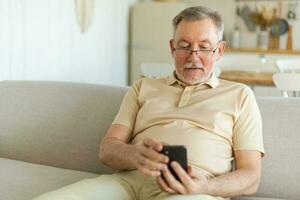 Happy middle aged senior man holding using smartphone touch screen typing scroll page. Stylish older mature beard grandfather with cell phone using internet social media apps at home. Shopping online. photo