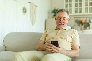 Happy middle aged senior man holding using smartphone touch screen typing scroll page. Stylish older mature beard grandfather with cell phone using internet social media apps at home. Shopping online. photo