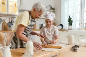 Happy family in kitchen. Grandmother and granddaughter child cook in kitchen together. Grandma teaching kid girl roll out dough bake cookies. Household teamwork helping family generations concept. photo