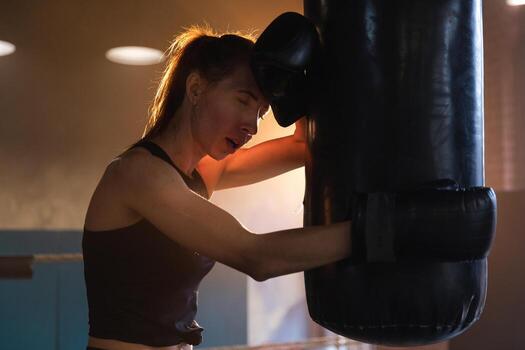 mujer yo defensa niña fuerza. fuerte mujer combatiente descansando después lucha formación en boxeo anillo. fuerte niña cansado después puñetazos boxeo bolsa. formación día en gimnasia. fuerza ajuste cuerpo rutina de ejercicio capacitación. foto