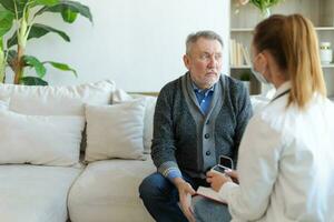 Female doctor examining older senior man in doctor office or at home. Old man patient and doctor have consultation in hospital room. Medicine healthcare medical checkup. Visit to doctor. photo