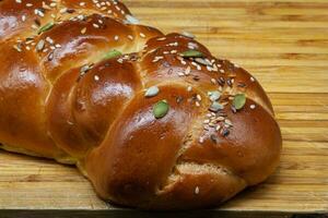 A white challah loaf on a wooden board with linseeds, sunflower seeds and pumpkin seeds. Golden freshly baked crust with highlights. Photo in high quality.