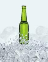 Green bottle of fresh beer with drops floats up through the ice cubes photo