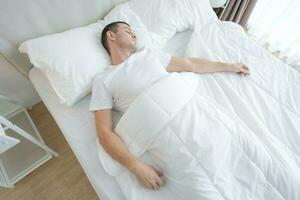 el joven hombre dormido en un cómodo blanco dormitorio. foto