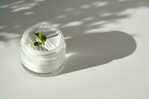 An open jar of facial scrub powder with a green sprig. photo