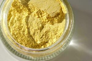 An open jar of a yellow turmeric facial scrub showing off its texture. photo