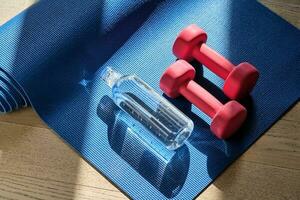 Reusable glass water bottle on a yoga mat with dumbbells. photo
