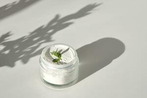 An open jar of facial scrub powder with a green sprig. photo