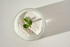 An open jar of facial scrub powder with a green sprig. photo