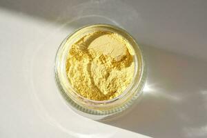 An open jar of a yellow turmeric facial scrub showing off its texture. photo