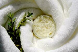 A jar of scrub wrapped in a terry bath towel with a green sprig. photo