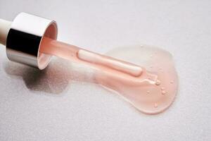 A pipette with a pink cosmetic lies in a drop. photo