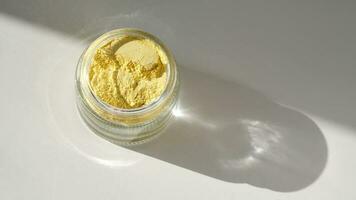 An open jar of a yellow turmeric facial scrub showing off its texture. photo