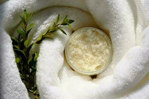 A jar of scrub wrapped in a terry bath towel with a green sprig. photo