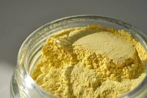 An open jar of a yellow turmeric facial scrub showing off its texture. photo