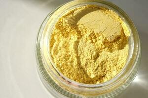 An open jar of a yellow turmeric facial scrub showing off its texture. photo