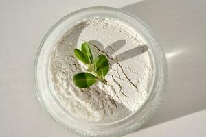 An open jar of facial scrub powder with a green sprig. photo