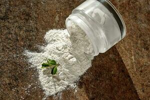 An open jar of facial scrub powder with a green sprig. photo