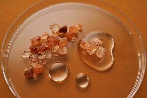 Three drops of liquid with pink salt on an orange background. photo