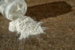 An open jar of facial scrub-powder scattered on a tile. photo