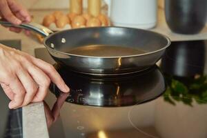 Woman turn on induction hob with frying pan photo