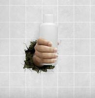 Human hand holding a cosmetics bottle through the wall with cracks photo