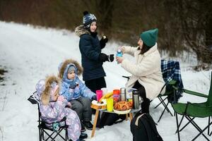 Young woman with children in winter forest on a picnic. Mother and three kids. photo