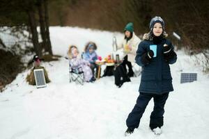 Boy with cup of tea at hand against his family in winter forest spending time together on a picnic. photo