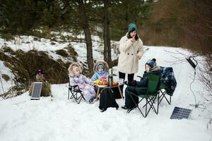 Young woman with children in winter forest on a picnic. Mother and three kids. photo