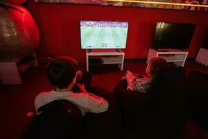 Two boys gamers play football gamepad video game console in red gaming room. photo