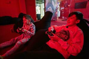 Two boys gamers play gamepad video game console in red gaming room. photo